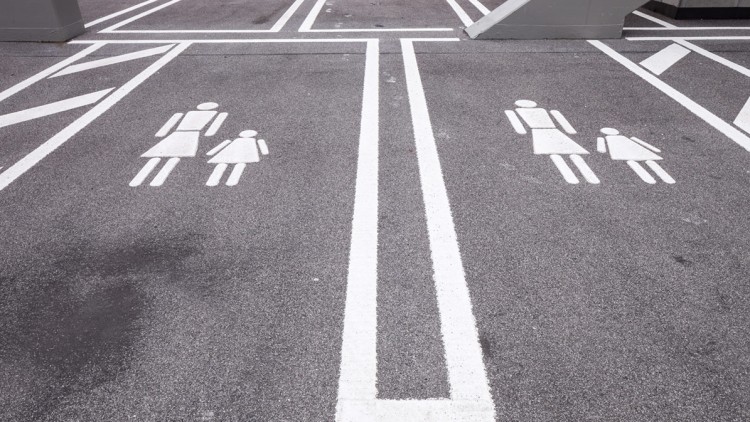 Markierungen auf einem Parkplatz mit Symbolen von zwei Erwachsenen und je einem Kind auf asphaltierter Fläche.