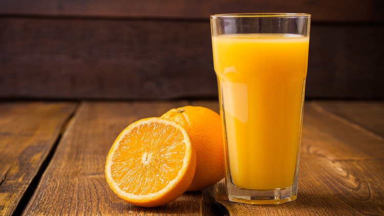 Ein gefülltes Glas Orangensaft steht neben zwei Orangen, eine davon aufgeschnitten, auf einem rustikalen Holzuntergrund.