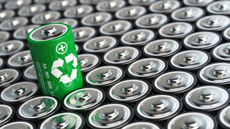 Eine grüne AA-Batterie mit Recycling-Symbol steht schräg auf einer Fläche aus silbernen Batterien.