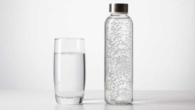 Ein Glas mit stillem Wasser steht neben einer Glasflasche mit Sprudelwasser auf einem weißen Untergrund.