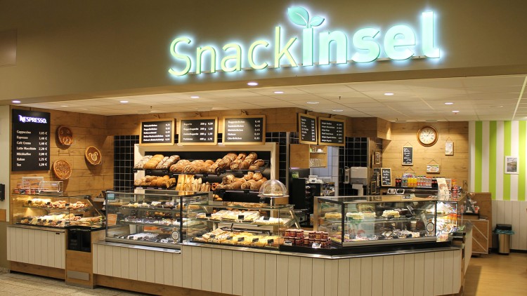 Brot- und Snacktheke mit vielfältigen Backwaren, Kuchen und belegten Brötchen, darüber der leuchtende Schriftzug Snackinsel.
