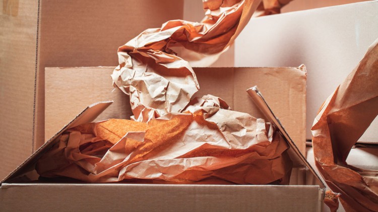 Geöffnete braune Kartons mit zerknülltem Packpapier in Orangetönen.