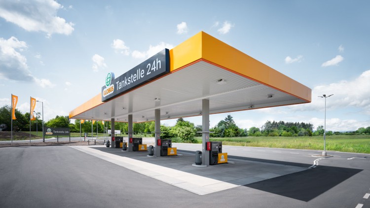 GLOBUS Tankstelle mit orange-gelbem Dach, der Aufschrift „Tankstelle 24h“ und mehreren Zapfsäulen auf einem freien Parkplatz.