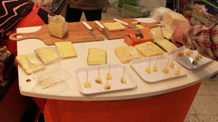 Mehrere Käsesorten auf Holzbrettern und Platten mit Probierstücken auf Zahnstochern an einem Verkostungsstand.