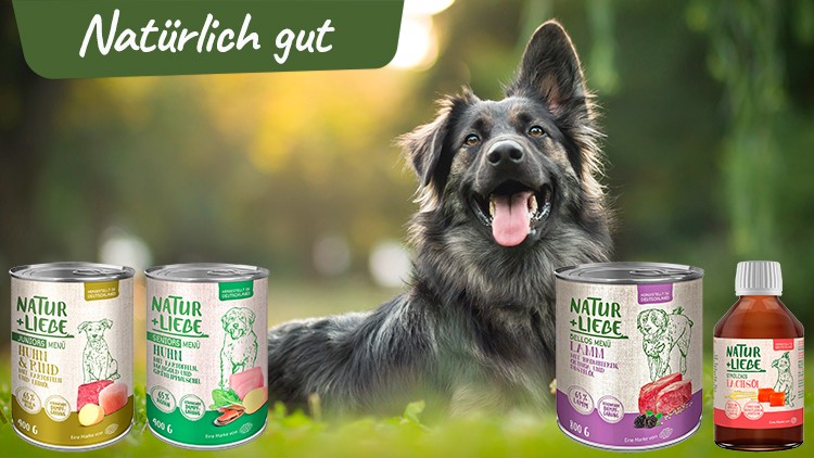 Ein schwarz-grauer Hund sitzt auf einer Wiese, umgeben von Natur + Liebe Hundennahrung und dem Schriftzug Natürlich gut.