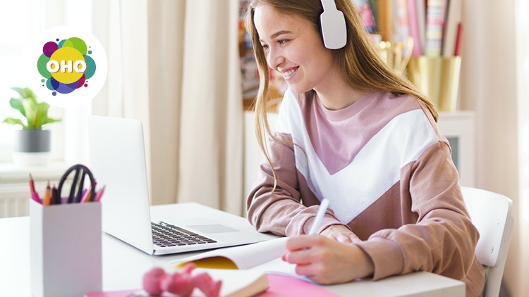 Person mit weißem Headset schreibt an einem Schreibtisch, vor ihr stehen ein Laptop, Stiftehalter und Bücher, Logo „OHO“ sichtbar.