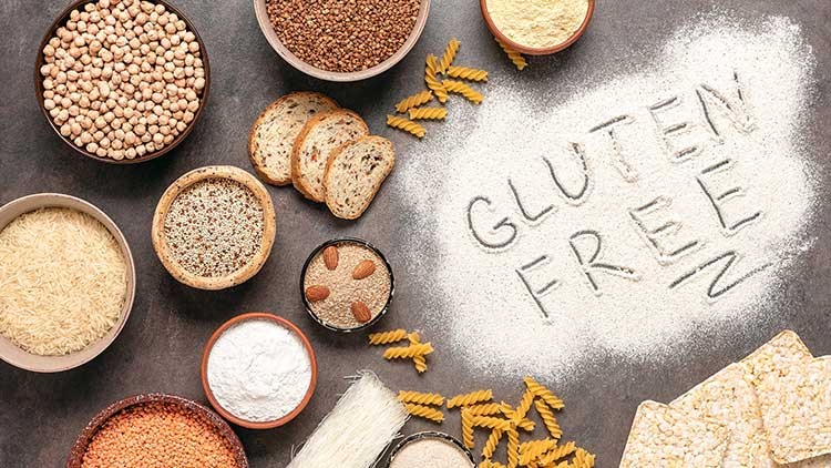 Verschiedene glutenfreie Lebensmittel wie Reis, Linsen, Hirse, Maismehl, Nudeln und Brot, Schriftzug „GLUTEN FREE“ in Mehl.