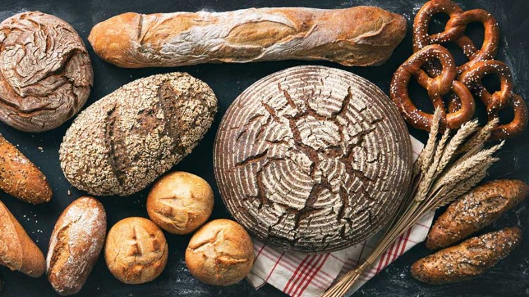 Verschiedene Sorten Brot und Gebäck wie Brezeln, Baguettes, Körnerbrote und ein Laib mit Muster auf dunklem Untergrund.