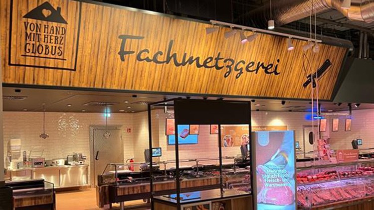 GLOBUS Fachmetzgerei mit Holz-Optik-Schriftzug, Glastheken voller Fleischwaren und Werbeschild mit Fleisch- und Wursthinweis.