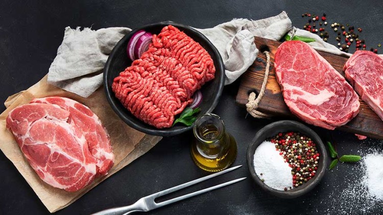 Verschiedene rohe Fleischsorten wie Rindersteak, Hackfleisch, Schweinefleisch und Hähnchenbrust auf schwarzem Untergrund mit Gewürzen.