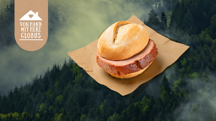 Ein Brötchen mit Leberkäs auf braunem Papier vor einem Hintergrund aus nebligem Wald, links Text: „Von Hand mit Herz GLOBUS“.