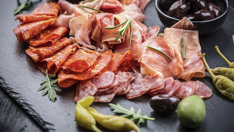 Auf einer Platte liegen verschiedene Wurst- und Schinkensorten mit Rosmarin, Oliven, Peperoni und Rucolablättern.