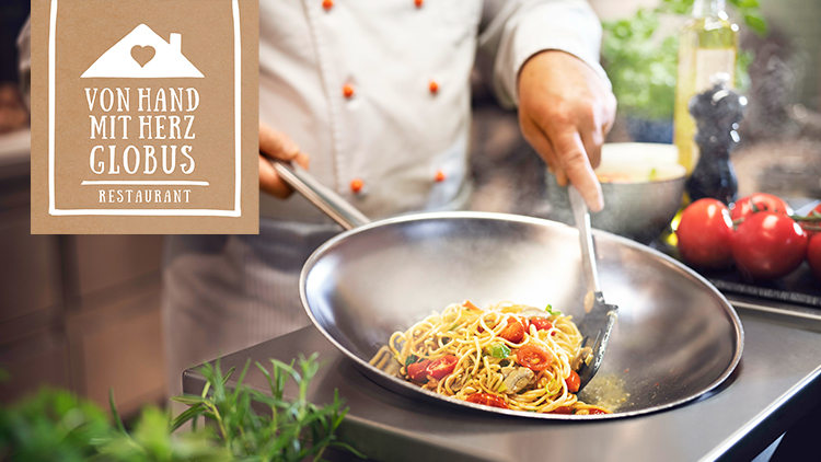 In einer Pfanne werden dampfende Nudeln mit Tomaten und Kräutern zubereitet, links oben steht „Von Hand mit Herz GLOBUS Restaurant“.