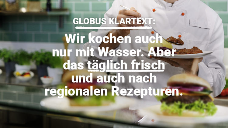 Ein Koch trägt weiße Kleidung und hält zwei Teller mit Speisen vor einer Küche mit grüner Kachelwand, Text: GLOBUS KLARTEXT:.