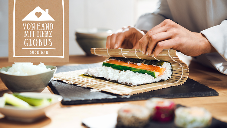 Hände rollen Sushi mit Lachs, Gurke, Reis und Nori auf Bambusmatte, daneben ein Schälchen Reis und Logo „Von Hand mit Herz GLOBUS Sushibar“.