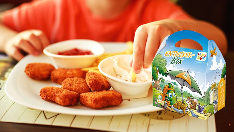 Ein Kind greift nach einer Pommes auf einem Teller mit Nuggets, Dip-Schälchen und einer Entdecker-Box mit Globini-Motiv.