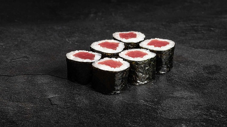 Sechs Stück Maki-Sushi mit weißem Reis, rohem Fisch und Algenhülle auf dunklem Untergrund.