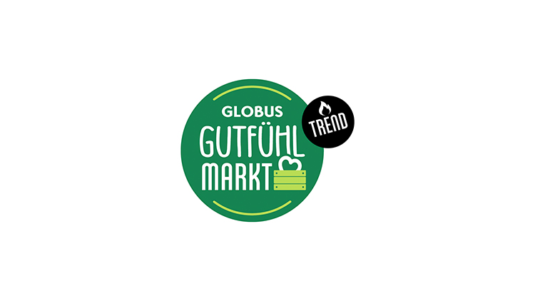 Grünes rundes Logo mit weißem Text „GLOBUS GUTFÜHL MARKT“, einem Herzsymbol, einer Holzkiste und einem schwarzen Kreis mit „TREND“.