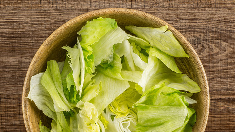 Grüner Eisbergsalat liegt in einer runden Holzschüssel auf einem braunen Holztisch.