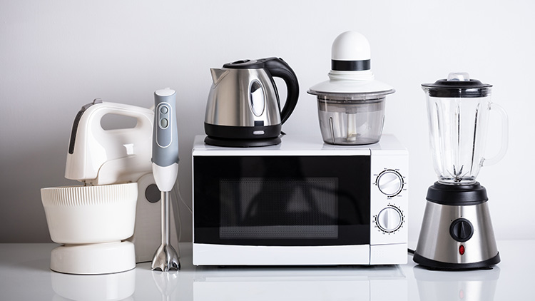 Fünf Küchengeräte, darunter Handmixer, Stabmixer, Wasserkocher, Zerkleinerer und Standmixer, stehen neben einer Mikrowelle.