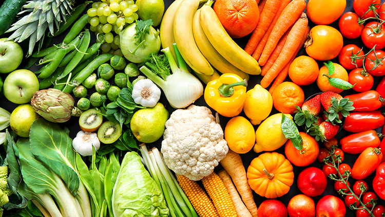 Frisches Obst und Gemüse in verschiedenen Farben wie grün, gelb, orange, rot, lila und weiß auf dunklem Untergrund.