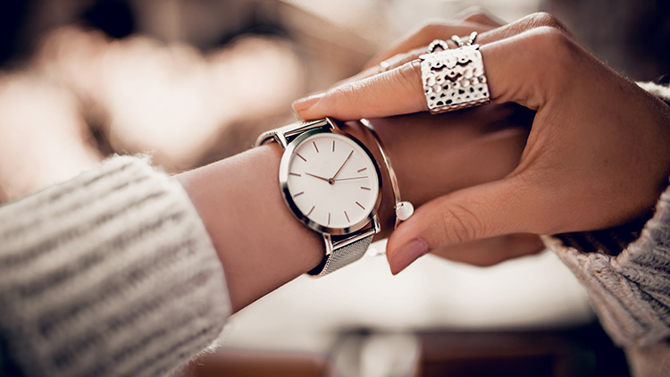 Eine silberne Armbanduhr mit weißem Zifferblatt wird an ein Handgelenk gelegt, umgeben von weichem Licht.
