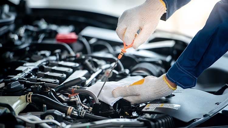Eine Person mit weißen Arbeitshandschuhen prüft den Ölstand eines Autos mit einem orangefarbenen Ölmessstab.
