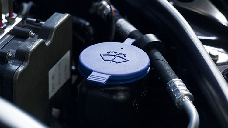 Ein blauer Deckel mit Scheibenwischersymbol sitzt auf einem Behälter im Motorraum eines Fahrzeugs.