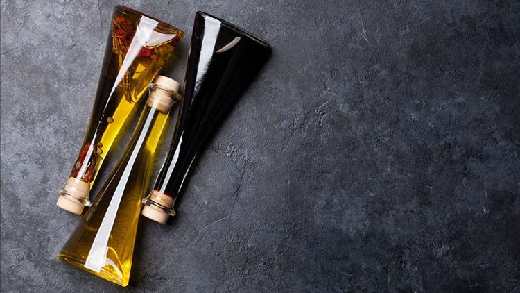 Zwei schlanke Glasflaschen mit goldgelbem und dunklem Inhalt liegen diagonal auf einer dunkelgrauen Steinoberfläche.