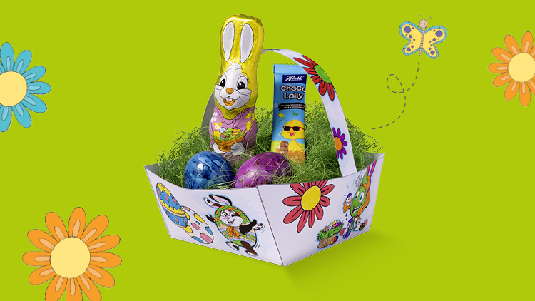 Ein bunter Osterkorb mit Schokohase, Schoko-Lolly und bemalten Eiern auf grünem Hintergrund mit Blumen und Schmetterling.