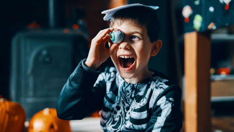 Kind in schwarzem Skelettkostüm sitzt, umgeben von geschnitzten Kürbissen und Halloween-Dekoration, in einem gemütlichen Raum.