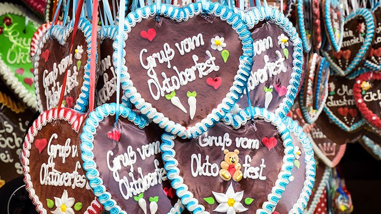 Mehrere Lebkuchenherzen mit blauer Zuckerverzierung und der Aufschrift „Gruß vom Oktoberfest“ hängen nebeneinander.