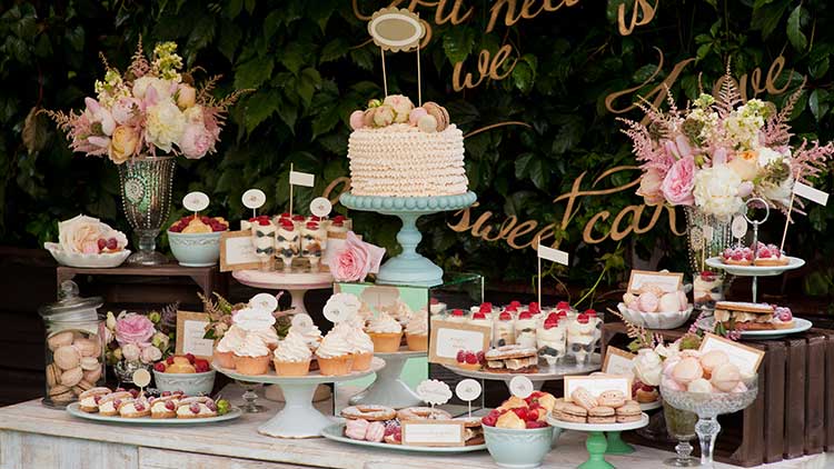 Eine festlich dekorierte Desserttisch mit Torte, Cupcakes, Macarons, Beeren und Blumen auf unterschiedlichen Etageren.