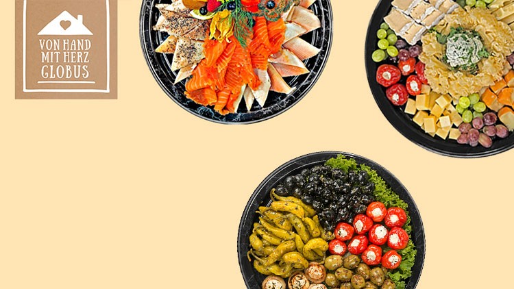 Drei runde Platten mit Lachs, Käse, Trauben, gefüllten Paprika und eingelegtem Gemüse, daneben ein „Von Hand mit Herz GLOBUS“-Schild.