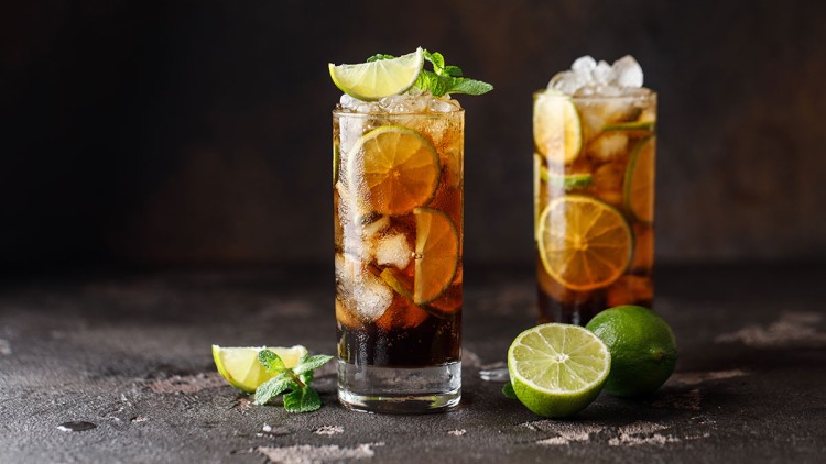 Zwei hohe Gläser mit Cola, Eiswürfeln, Limettenscheiben und Minzblättern, davor ganze und halbierte Limetten.