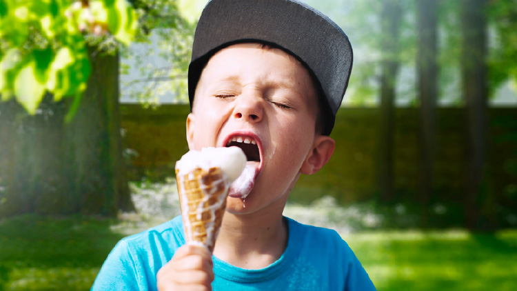Person mit grauer Kappe hält ein Eis in der Hand, im Hintergrund Bäume und unscharfe grüne Natur.