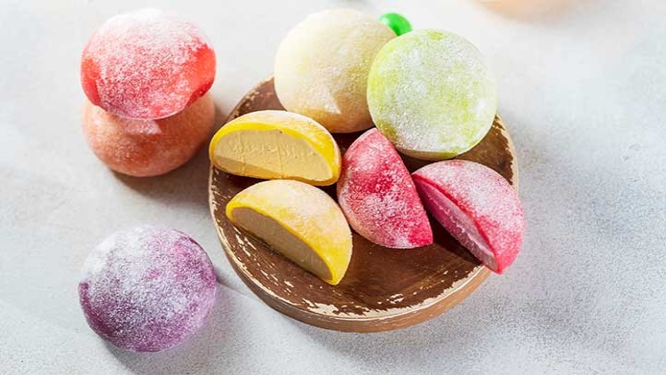 Bunte runde gefrorene Mochi-Desserts liegen auf einem Holzbrett, teils halbiert und mit eisiger Füllung sichtbar.