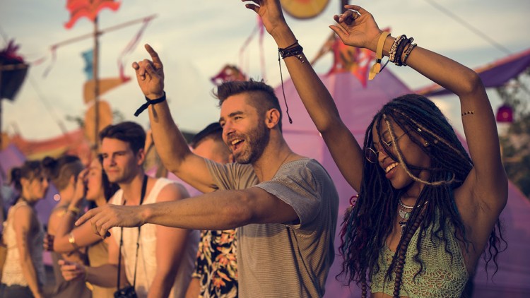 Menschen tanzen und heben die Arme auf einem Festival mit bunten Dekorationen und sommerlichem Ambiente.