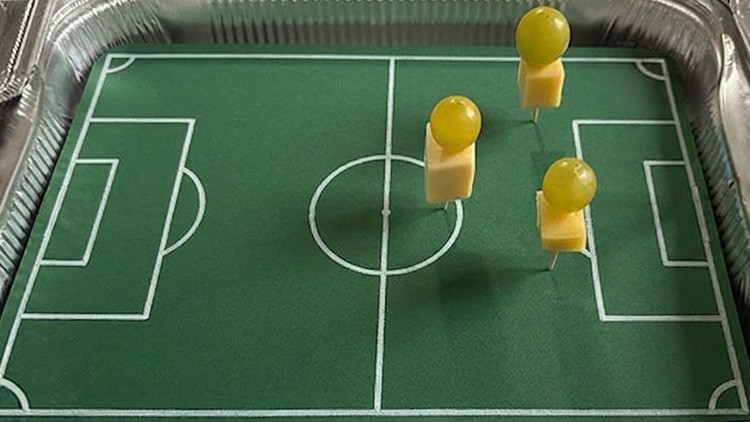 Grüne Fußballfeld-Dekoration in einer Aluschale mit Figuren aus Käsewürfeln und grünen Trauben auf Zahnstochern.