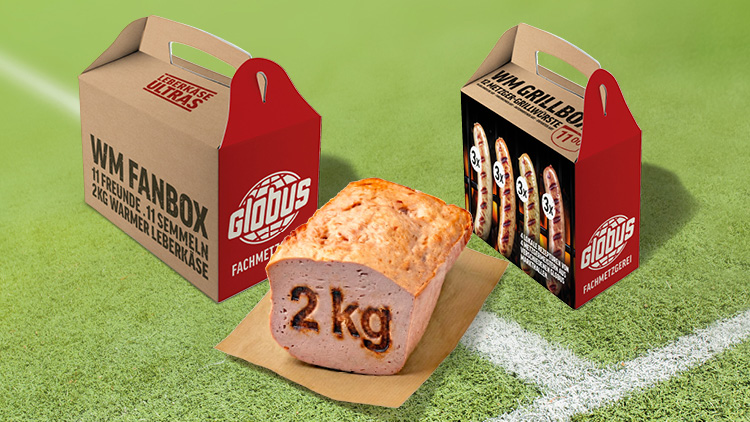 Grüne Rasenfläche mit zwei Boxen der GLOBUS Metzgerei und 2 kg Leberkäse auf einem Holzbrett, Texte auf den Boxen gut lesbar.