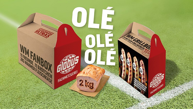 Zwei GLOBUS Boxen mit Fleischprodukten auf grünem Hintergrund, Text „OLÉ OLÉ OLÉ“ und „WM FANBOX“ sowie „WM GRILLBOX“ sichtbar.