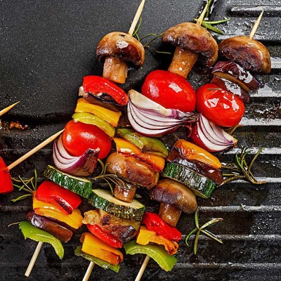 Gemüsespieße mit Paprika, Zucchini, Champignons, Tomaten und Zwiebeln sowie Fleischspieße auf einer heißen Grillplatte.