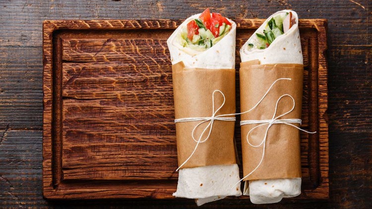 Zwei Wraps mit Gemüsefischfüllung liegen in braunem Papier eingewickelt und mit weißer Schnur gebunden auf einem Holztablett.