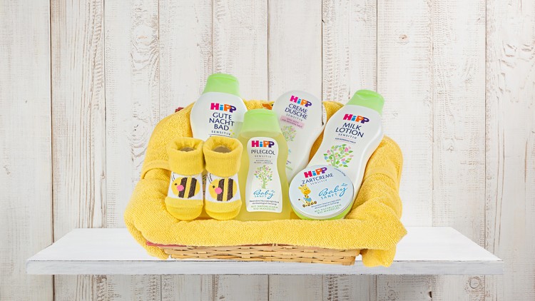 Ein gelber Korb enthält gelbe Babysocken, ein gelbes Handtuch und fünf HIPP Baby Produkte mit der Aufschrift „sensitive“.