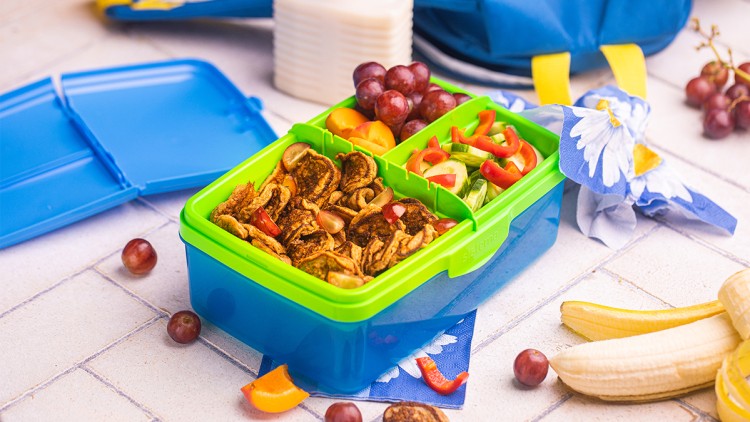 Blaue Lunchbox mit grünem Deckel enthält Mini-Pfannkuchen, Weintrauben, Paprika, Gurkenscheiben und Aprikosenstücke.