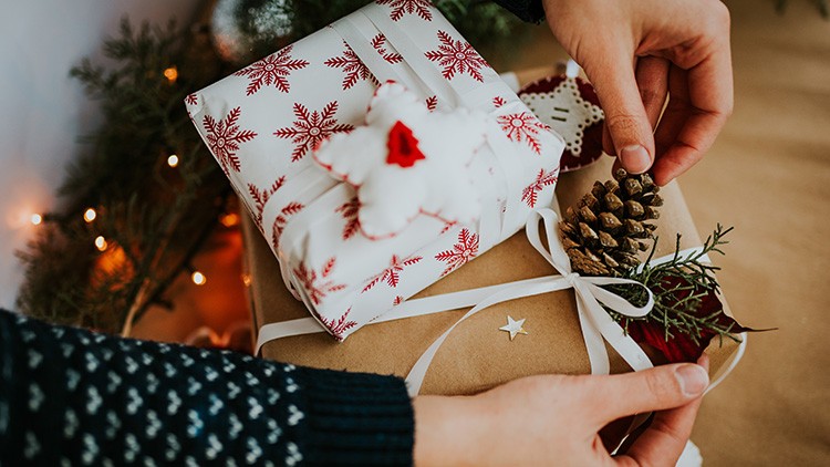 Zwei weihnachtlich verpackte Geschenke mit Dekoration aus Zweigen und Tannenzapfen werden von zwei Händen gehalten.