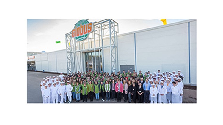 Eine große Gruppe von Mitarbeitenden steht vor dem Eingang eines GLOBUS Marktes mit Logo über der Tür.