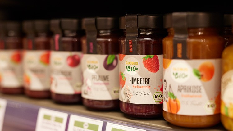 Gläser mit GLOBUS Bio Fruchtaufstrich in verschiedenen Sorten wie Himbeere, Pflaume und Aprikose in einem Regal.