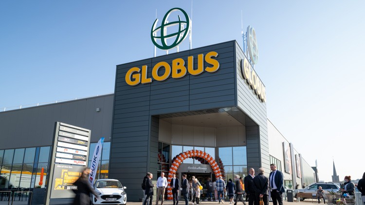 Das GLOBUS-Gebäude mit orangem Schriftzug und Eingang, dekoriert mit einem Bogen aus Luftballons, Menschen davor.