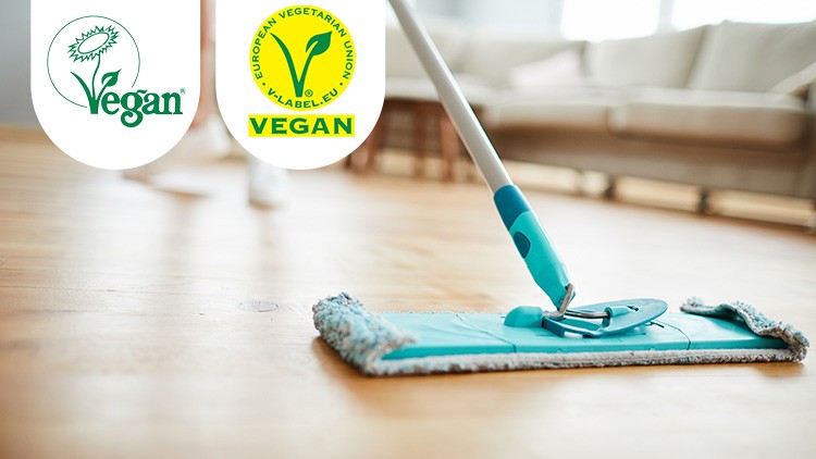 Ein türkisfarbener Wischmopp reinigt einen Holzfußboden, oben links zwei vegane Labels der Vegan Society und V-Label EU.